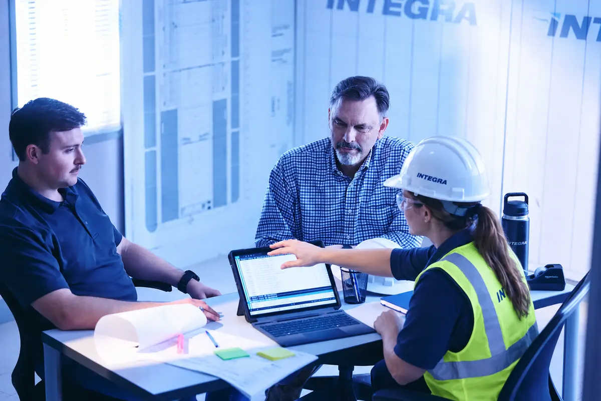 Three Integra staff reviewing drawings and a tablet around a meeting table