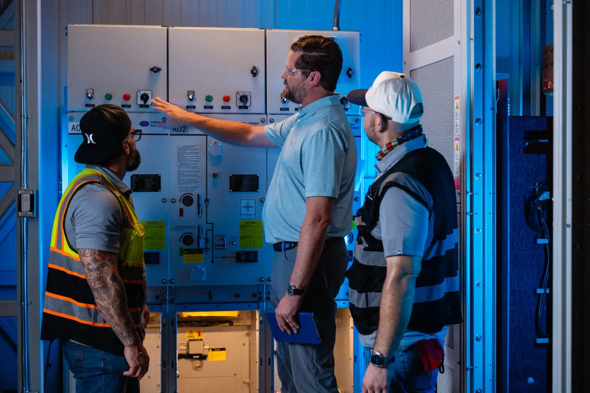 Three Integra staff inspecting an electrical control panel