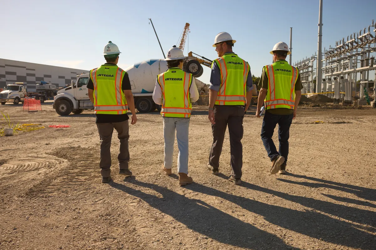 Four Integra workers in hard hats and hi-vis vests walking across the construction site